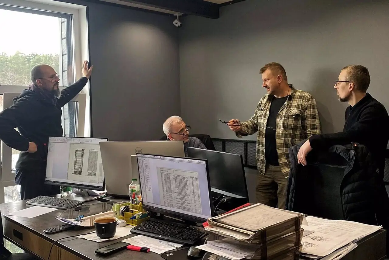 Zespół konstruktorów i inżynierów omawiający projekty CAD i rysunki techniczne w biurze projektowym.